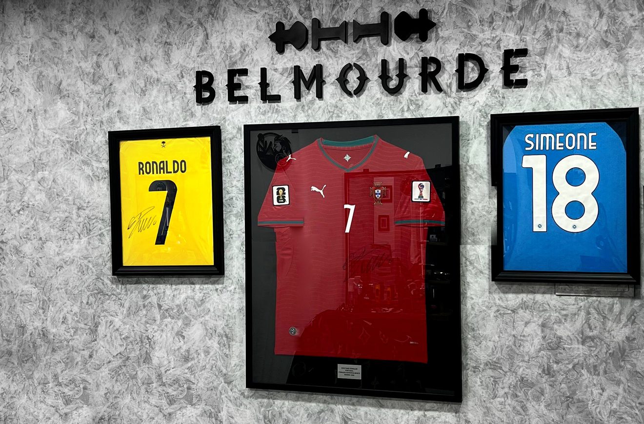Rincón del Salón de la Fama en Belmourde Barbería: rótulo Belmourde en relieve sobre tres camisetas firmadas y enmarcadas