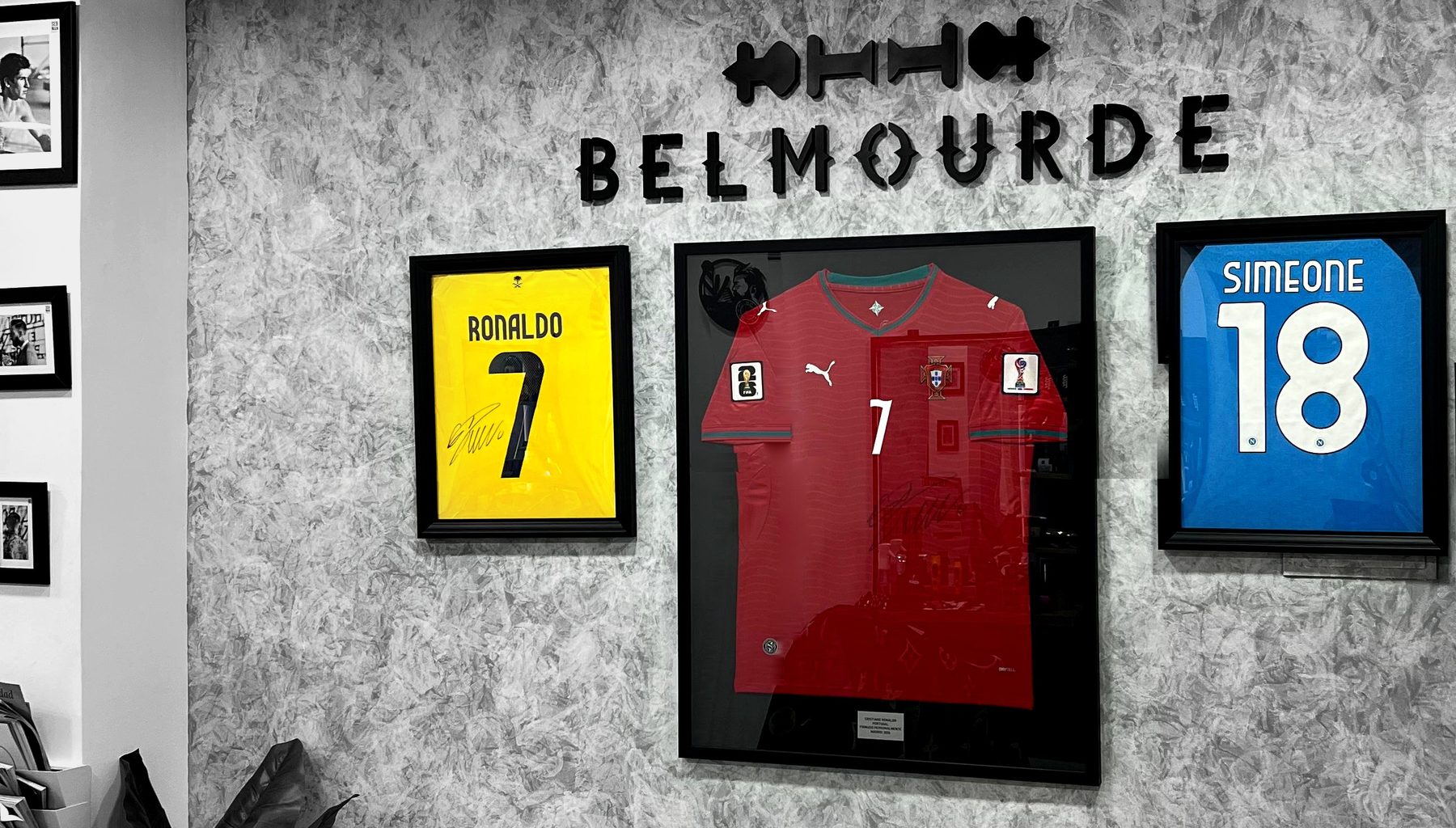Pared del Salón de la Fama de Belmourde Barbería: el rótulo en relieve y las camisetas firmadas y enmarcadas
